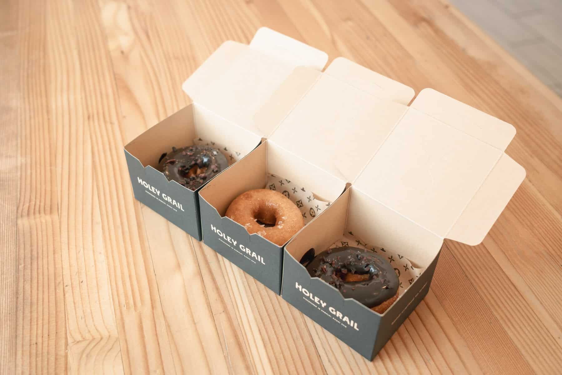 三個 Holey Grail Donuts 的甜甜圈分別裝在印有品牌標誌的紙盒中